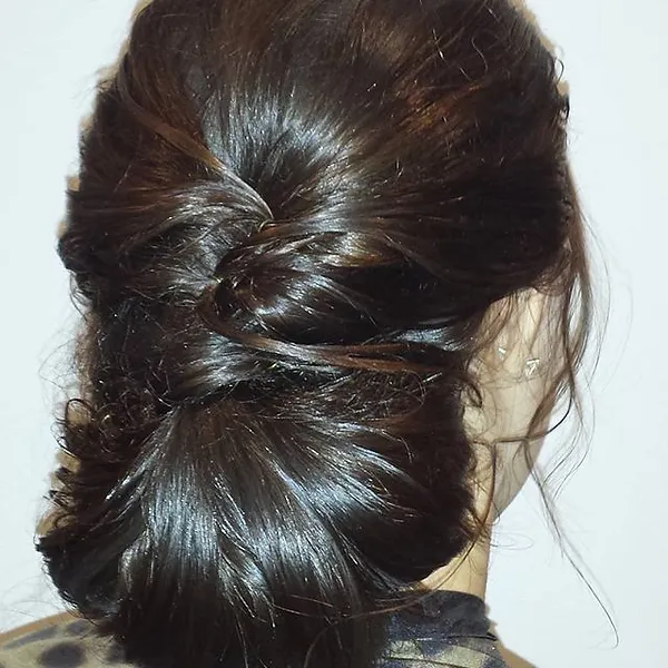 The back view of a person with dark brown hair styled in an elegant twisted bun, set against a plain white background